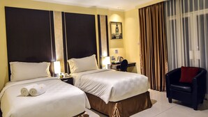 A hotel room with two beds, a desk, a chair, and a large window with curtains. - Sunbreeze Hotel Senayan (Jakarta)