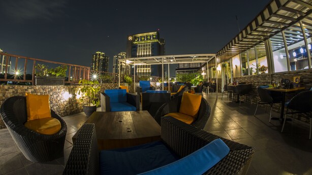 An outdoor seating area with wicker furniture and cushions, a stone wall, and a view of the city skyline at night. - Sunbreeze Hotel Senayan (Jakarta)