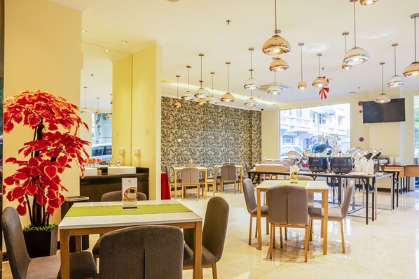 A modern dining area with multiple tables and chairs, a large potted plant, and a patterned wall. - Sunbreeze Hotel Senayan (Jakarta)