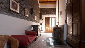 A room with a stone wall, wooden ceiling beams, a fireplace, and a large wooden cabinet. - Agriturismo Case Perrotta (Sant'Alfio)