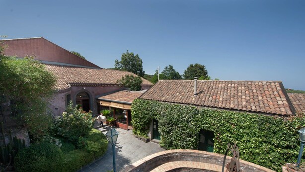 A courtyard with a building covered in ivy, a stone archway, and a clear blue sky. - Agriturismo Case Perrotta (Sant'Alfio)