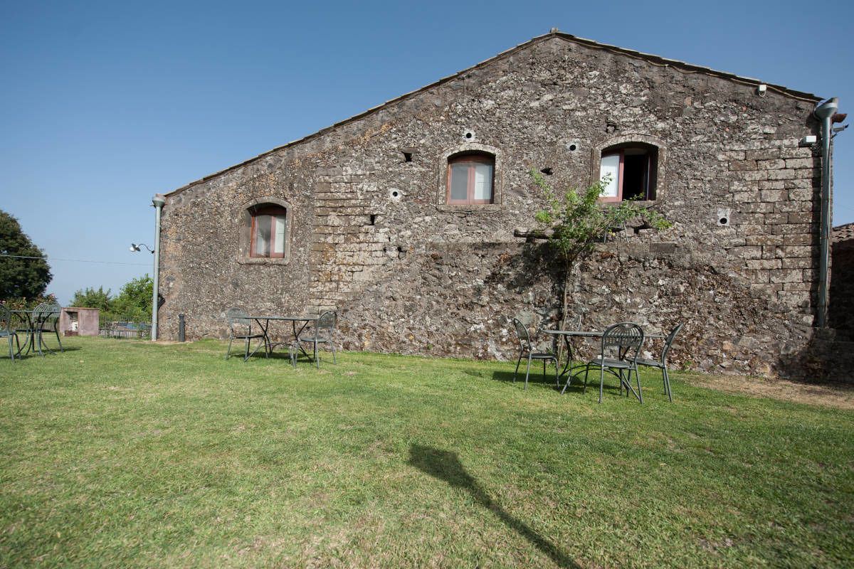 A rustic stone building with three windows, a small tree in front, and a grassy lawn.
