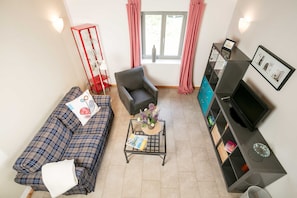 Una sala de estar con sofá, sillón, mesa de centro, mueble para televisión y una ventana con cortinas.