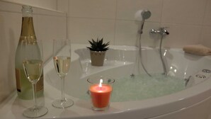 A bathtub with a lit candle, a bottle of champagne, and two glasses on a white surface. - Apartment Nice view - Ferienhof Börsby - Apartment Schöne Aussicht (Pommerby)