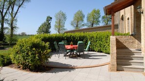 An outdoor patio with a table and chairs, surrounded by greenery and a brick wall. - Apartment Nice view - Ferienhof Börsby - Apartment Schöne Aussicht (Pommerby)