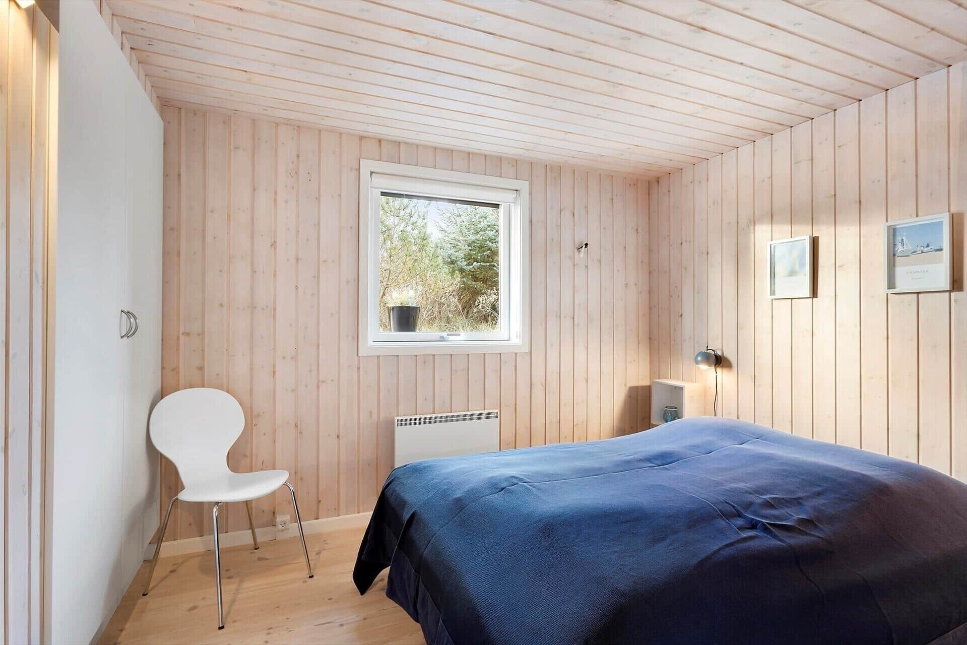 A bedroom with wooden walls, a single bed, a chair, a window, and a radiator.
