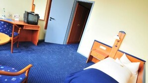 A hotel room with a bed, a desk with a television, a chair, and a small table. - Single room 03 - Hotel Goldene Krone (Clausthal-Zellerfeld)