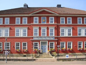 Een rood gebouw met witte details, een centrale ingang en bloembakken onder de ramen.