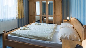 Ein Schlafzimmer mit einem hölzernen Bett, einem Schrank, einem Nachttisch mit Lampe und einem Fenster mit Vorhängen.