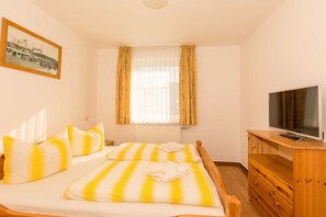 Une chambre à coucher avec un lit, une télévision, une commode en bois et une fenêtre avec des rideaux.
