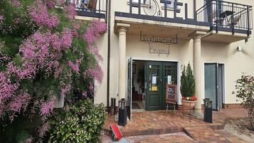A restaurant with a balcony, a sign above the entrance, and a flower pot on the ground.