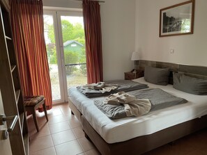Een slaapkamer met een groot bed, een nachtkastje, een stoel, een schuifdeur en een lijst met een afbeelding aan de muur.