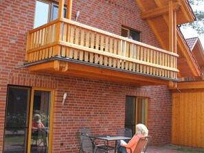 Un bâtiment à deux étages doté d’un balcon en bois, de murs en briques et d’un patio aménagé avec des chaises et une table en métal.