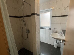 Une salle de bain avec une douche, un lavabo et une fenêtre.