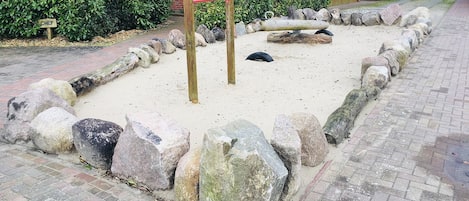 Zona de juegos arenosa con rocas grandes y un conjunto de columpios de madera.