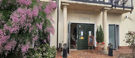 A restaurant with a balcony, a sign above the entrance, and a flower pot on the ground.