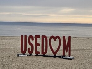 Ein Strand mit großen Buchstaben, die 'USEDOM' buchstabieren, und zwei Ortsangaben: KARLSHAGEN und TRASSENHEIDE.
