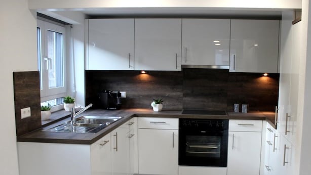 Eine moderne Küche mit weißen Schränken, einer dunkel gefliesten Rückwand und einem eingebauten Backofen.