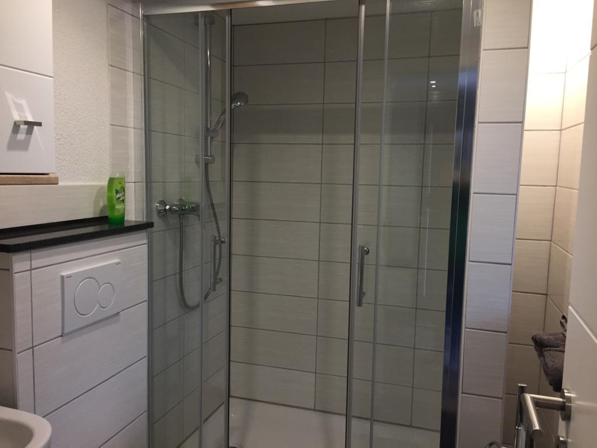 A modern bathroom with a glass-enclosed shower, white tiled walls, and a countertop with a soap dispenser.