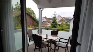 Ein Balkon mit Tisch und Stühlen, eine Glastür und Blick auf Häuser im Hintergrund.