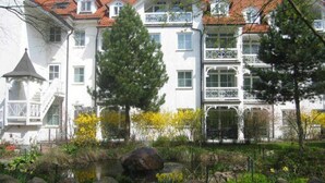 A multi-story building with balconies, a garden with rocks and plants, and a pond.