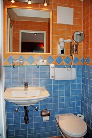Et badeværelse med vask, spejl, hårtørrer og toilet.