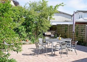 Une terrasse extérieure avec une table et des chaises, entourée de verdure et d’une clôture en bois.