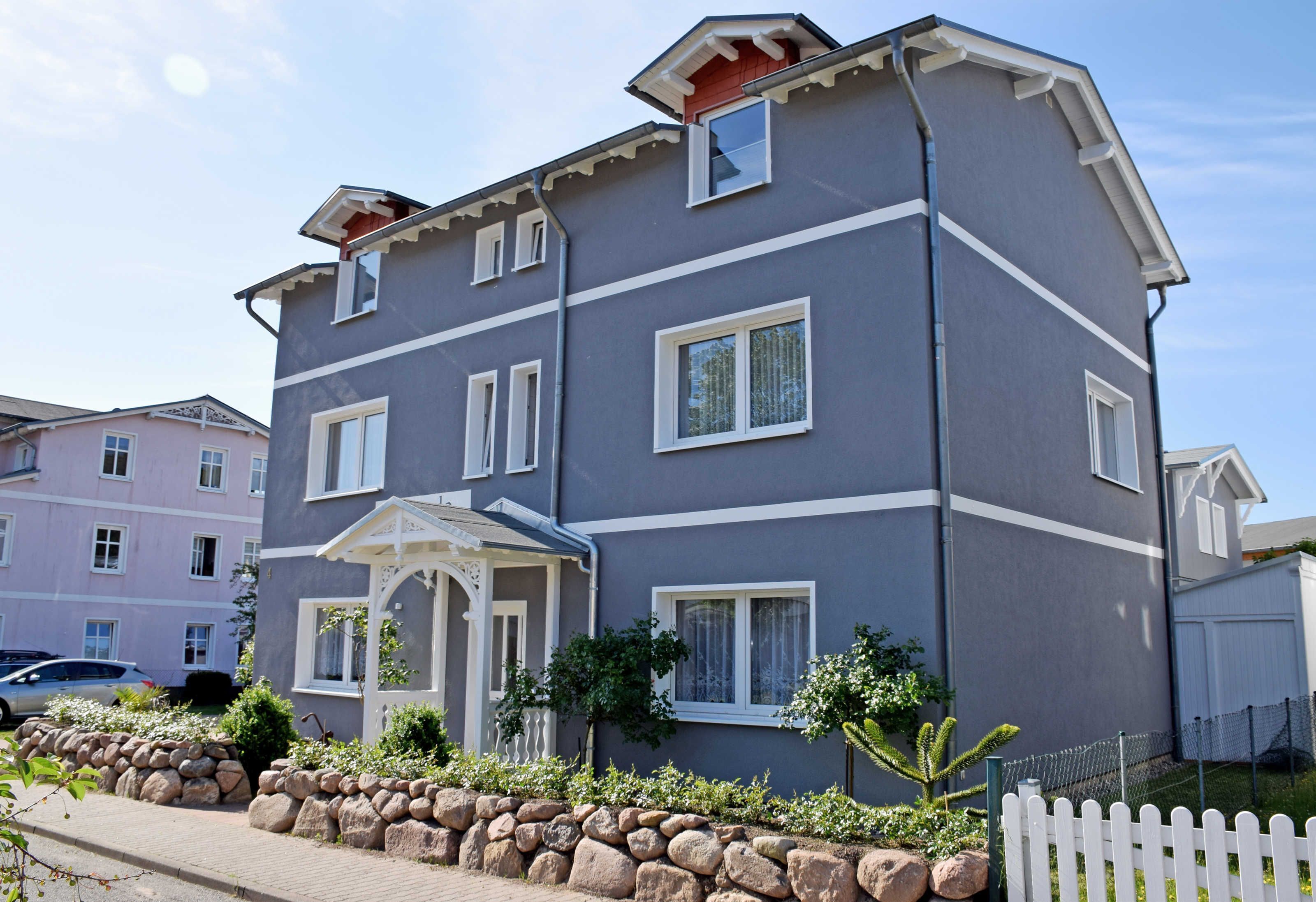 A multi-story residential building with a grey facade, white trim, and a small porch area.