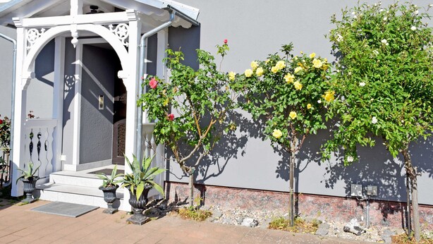 A building with a white entrance canopy, potted plants, and climbing roses. - Ferienappartement 02 - Pension/holiday apartments in the Ostseebad Sellin (Sellin)