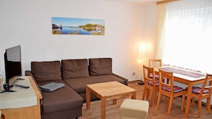 A living room with a sofa, a small wooden table, a TV, and a dining table with chairs. - Ferienappartement 02 - Pension/holiday apartments in the Ostseebad Sellin (Sellin)