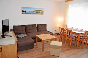 A living room with a sofa, a small wooden table, a TV, and a dining table with chairs.