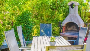 A wooden table with chairs, a potted plant, and a stone-built outdoor oven. - Ferienappartement 02 - Pension/holiday apartments in the Ostseebad Sellin (Sellin)