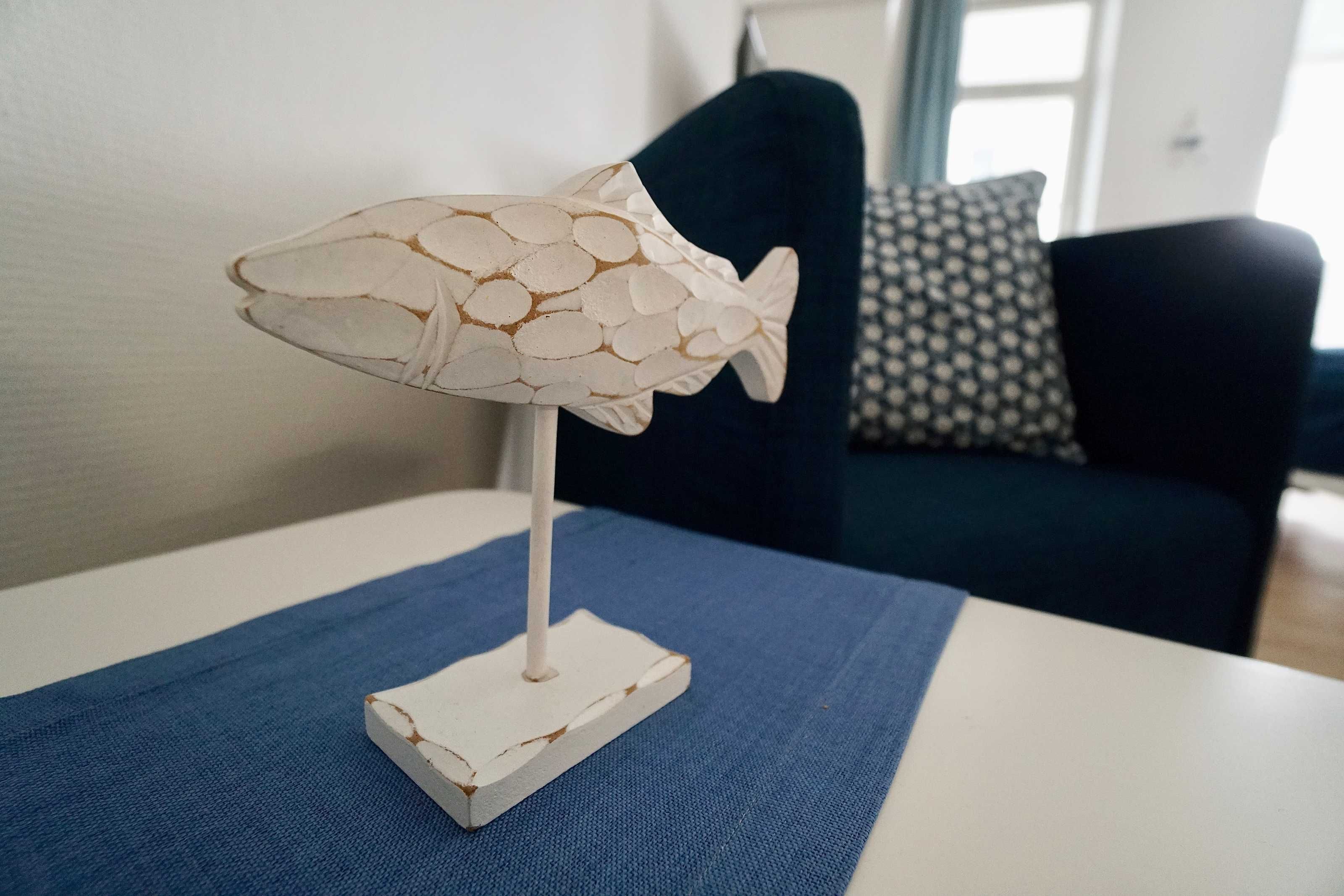 Luminária decorativa em formato de peixe sobre uma mesa branca com um tecido azul.
