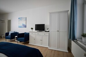 A modern bedroom with a bed, two blue armchairs, a TV, a white wardrobe, and a painting on the wall. - 09 Holiday apartment Granitz (A) - Apartment house Haus Arkona (Sellin)