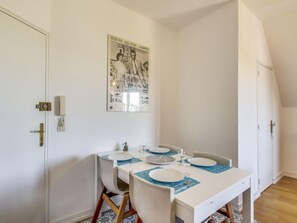 Comedor con una mesa blanca para cuatro, un cartel en la pared y una puerta a la izquierda.