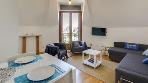 A living room with a dining area, a sofa, a TV, and a balcony with a view. - Basse Vallée by Interhome (Dinard)