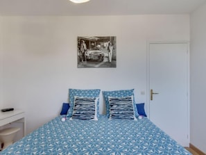 Un dormitorio con cama, dos almohadas, una mesita de noche, un control remoto y una puerta.