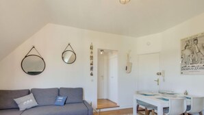 A modern living room with a grey sofa, a small white table, and a dining area with a white table and chairs. - Basse Vallée by Interhome (Dinard)