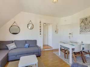 Een moderne woonkamer met een grijze bank, een klein wit tafeltje en een eethoek met een witte tafel en stoelen.
