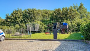 A paved area with a playground, a fence, and a vehicle.
