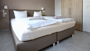 A modern hotel room with a large bed, two bedside tables, a wardrobe, and a wall-mounted lamp.