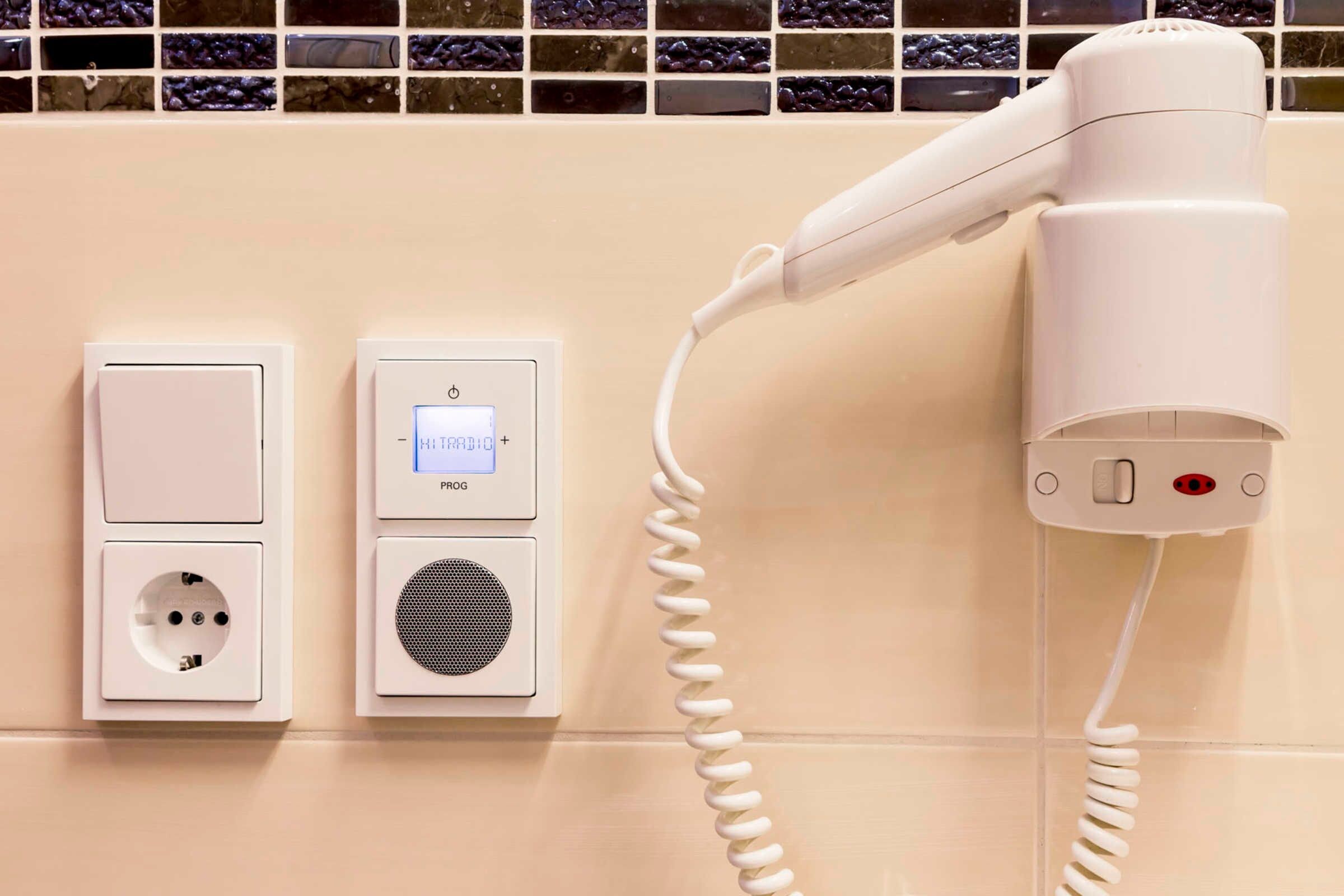 A hairdryer plugged into a wall socket with a control panel displaying 'PIRG' and a power button.