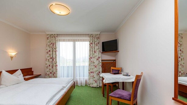 Une chambre d’hôtel comprenant un lit, un bureau avec une chaise, une télévision et une fenêtre avec des rideaux.