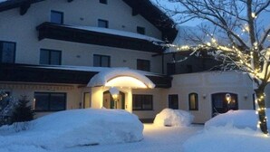 Un hôtel dont l’entrée est recouverte de neige, qui possède un porche abrité et un arbre décoré de guirlandes lumineuses.