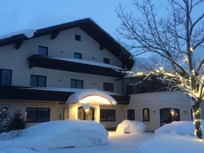 Ein Hotel mit verschneitem Eingangsbereich, einer Veranda und einem Baum mit Lichterketten.