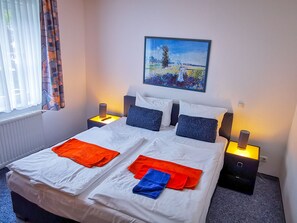 Ein Doppelbett mit weißen Leinentüchern, zwei Kissen und einer Decke. Zwei Nachttische mit Lampen stehen bereit. Über dem Bett hängt ein Gemälde.