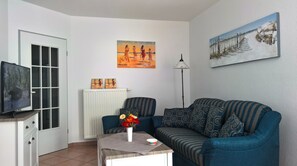 A living room with a television, a sofa, a coffee table with flowers, and two paintings on the wall.