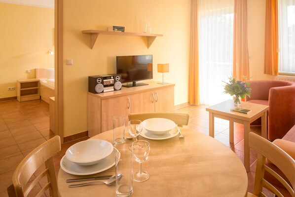 Un coin repas avec une table en bois dressée pour deux personnes, un téléviseur posé sur un meuble en bois et un fauteuil rouge.