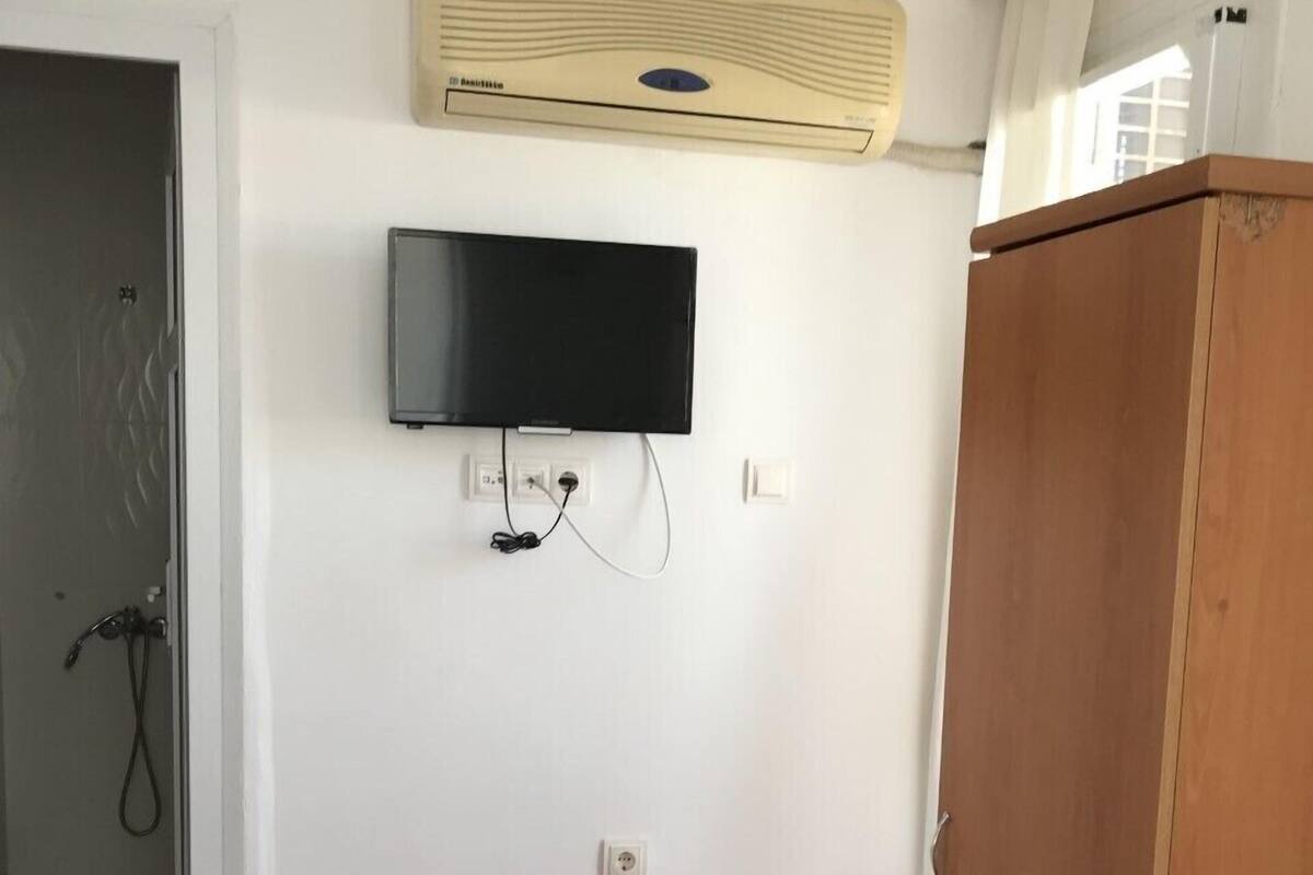Ein Zimmer mit an der Wand montiertem Fernseher, einem Holzschrank und einem roten Teppich mit Muster.