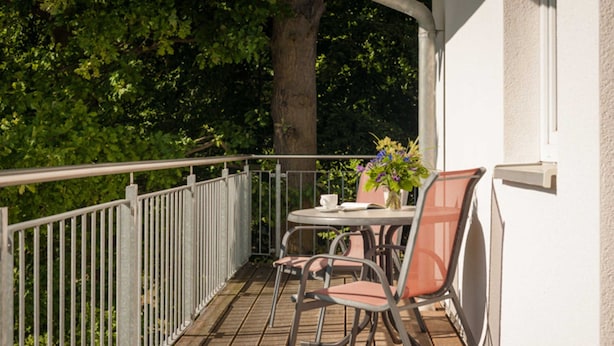 A balcony with a table and chairs, surrounded by a metal railing, and a tree in the background. - Vacation apartment WE10 - Holiday apartments at the sports field (Sellin)